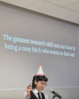 A picture of a person doing a presentation with a party hat on their head with a slide behind them saying 'The greatest research skill you can have is being a nosy bitch who wants to find out'