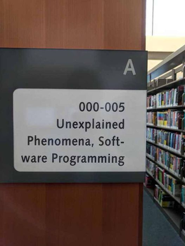A sign indicating the bookshelf's category in a library which says '000-005 Unexplained Phenomena, Software Programming'